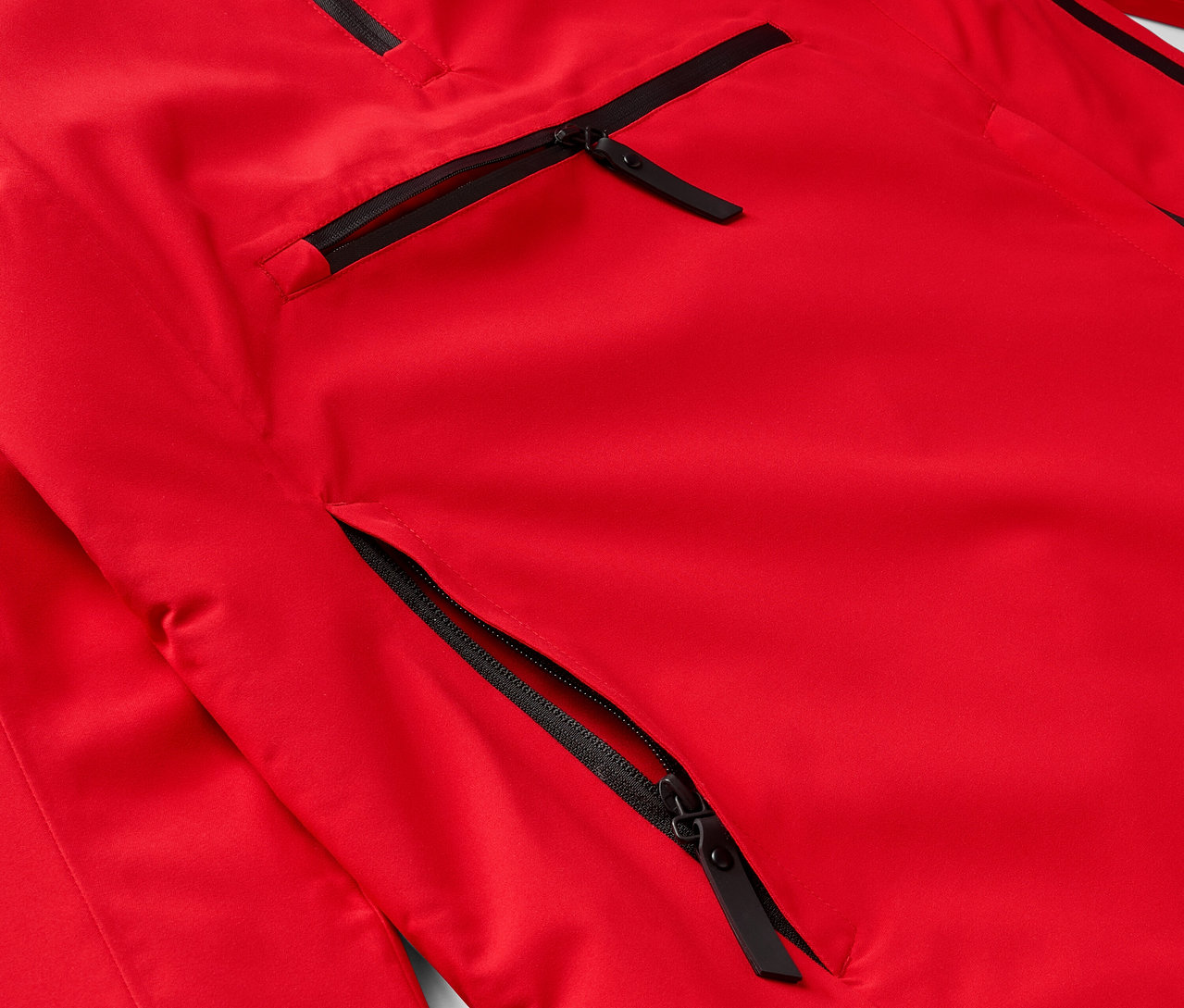 Détail d'une veste rouge avec des fermetures éclair noires sur les poches.