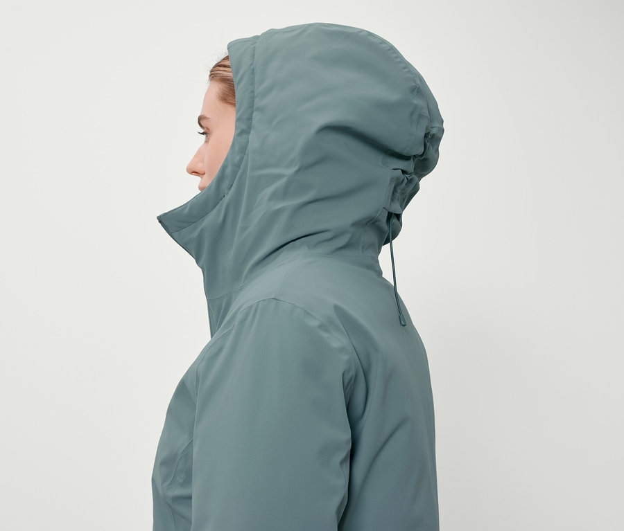 Profil d'une femme portant un manteau à capuche bleu-vert sur un fond blanc.