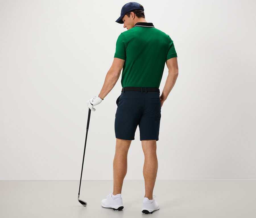 Un homme en polo vert et short fonctionnel tient un club de golf.