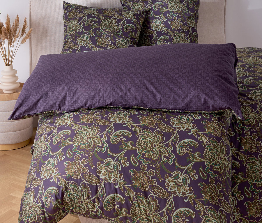 Un lit avec des draps violets à motifs floraux et deux oreillers.