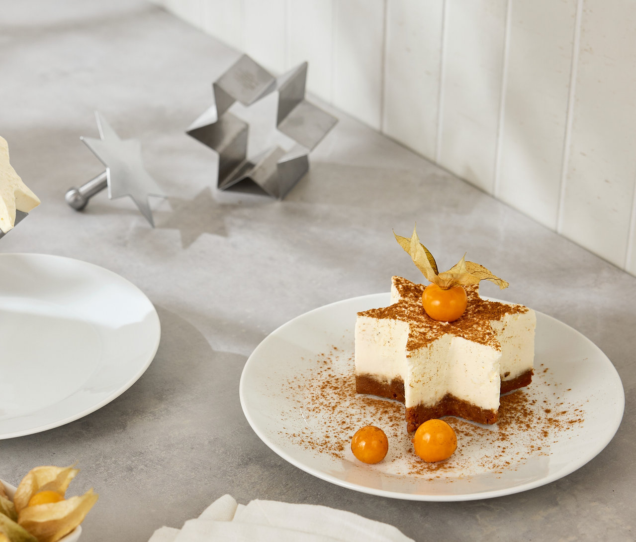 Gâteau en forme d'étoile avec des physalis sur une assiette blanche à côté d'emporte-pièces en forme d'étoile.