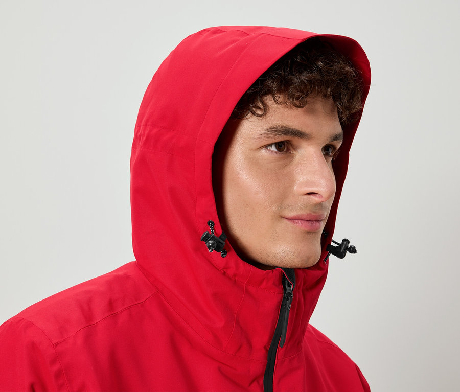 Un homme aux cheveux bouclés porte une veste rouge à capuche.