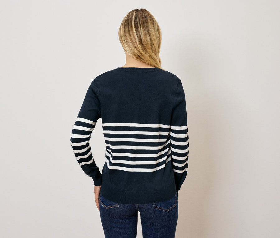 Vue de dos, une femme aux cheveux blonds porte un pull rayé bleu et blanc et un jean.