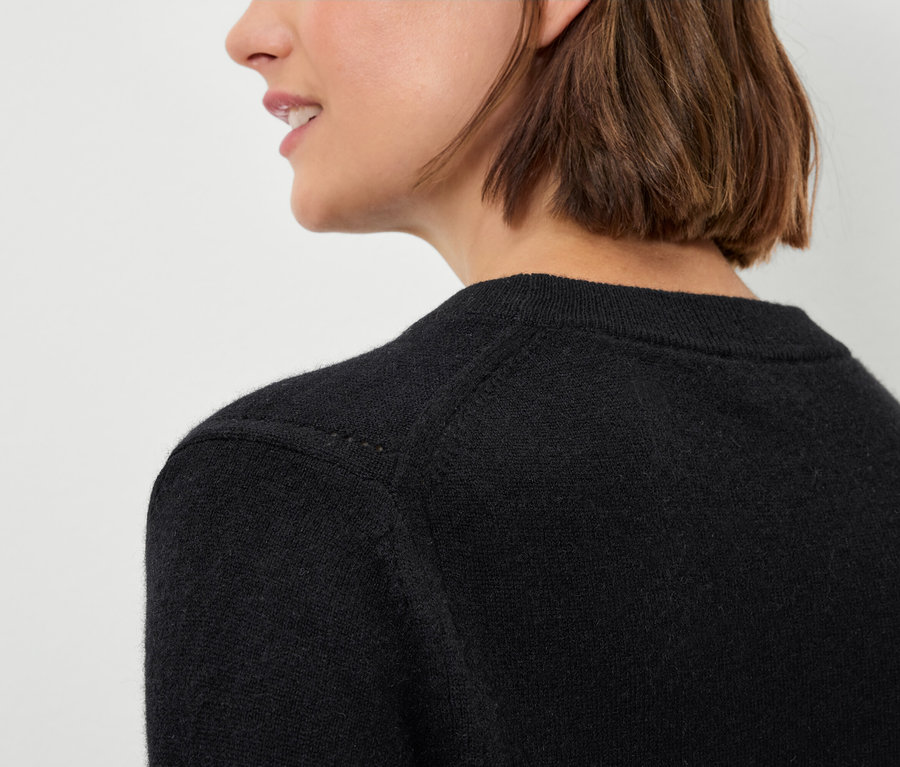 Détail d'un pull noir pour femme sur une femme aux cheveux bruns.