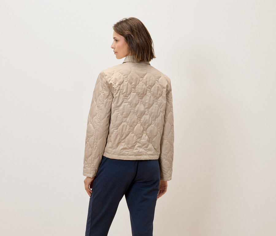Une femme, dos à la caméra, porte une veste matelassée beige et un pantalon bleu.