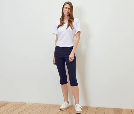 Une femme debout portant un pantalon 3/4 en bengaline bleu foncé, un t-shirt blanc et des baskets.