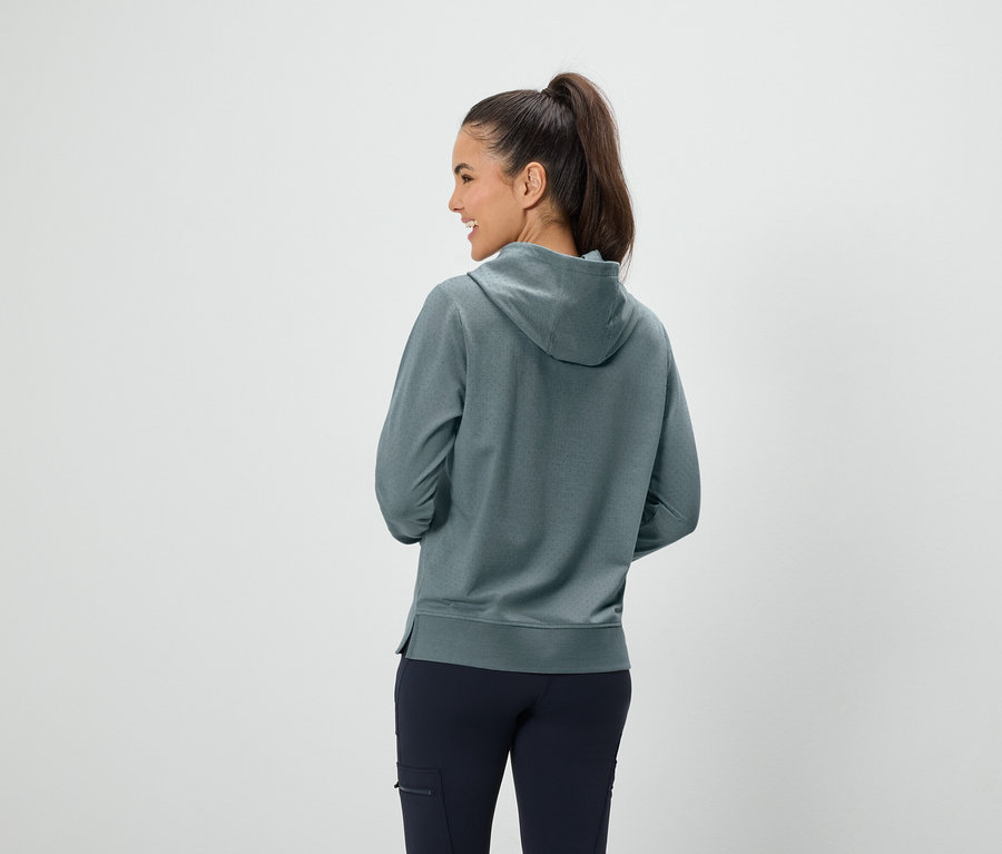 Une femme aux cheveux bruns attachés en queue de cheval se tient dos à la caméra et porte un sweat à capuche bleu-vert et un pantalon bleu foncé.