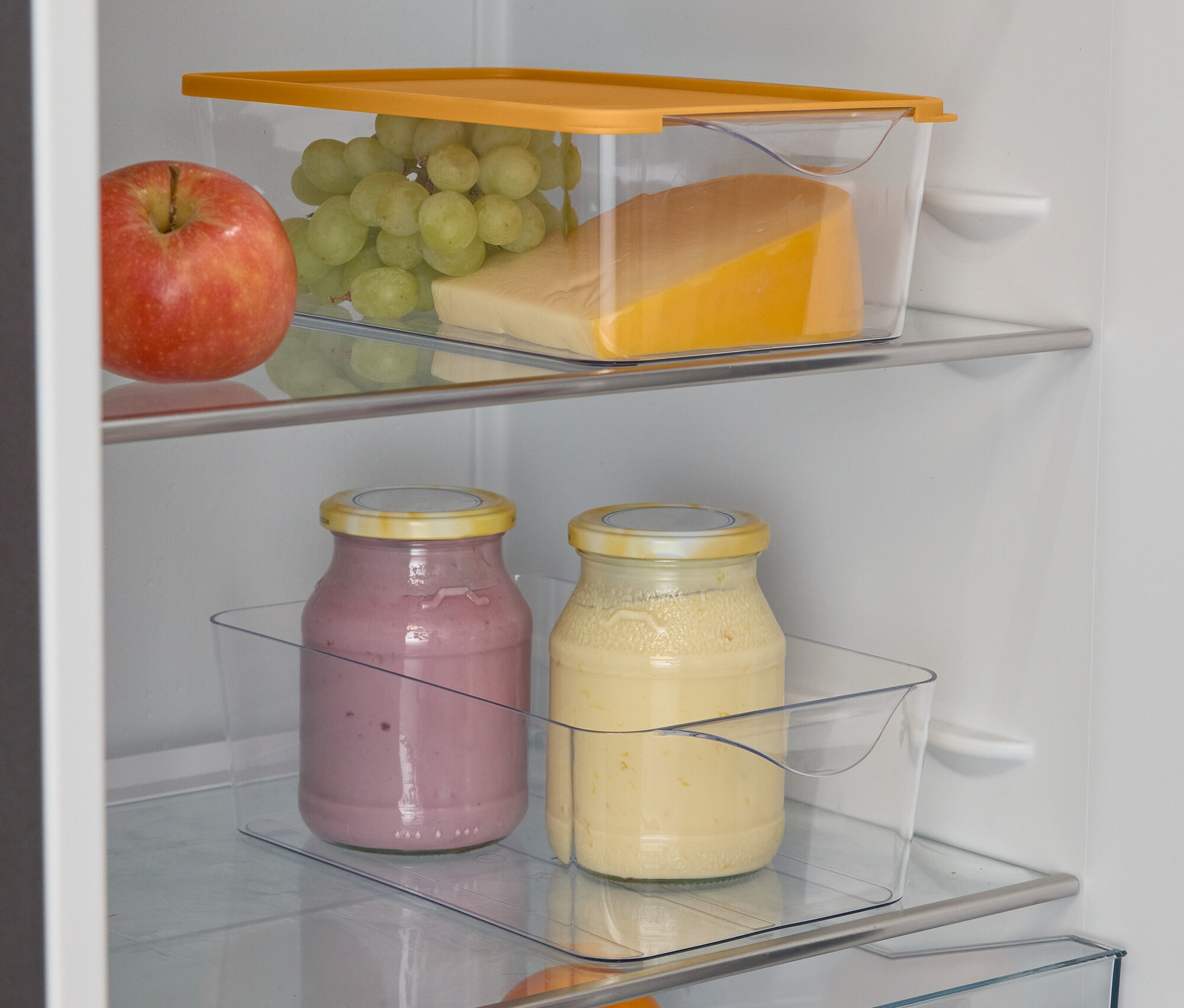 Un réfrigérateur ouvert avec une pomme, des raisins, du fromage, deux verres de smoothie, une orange et des limes.