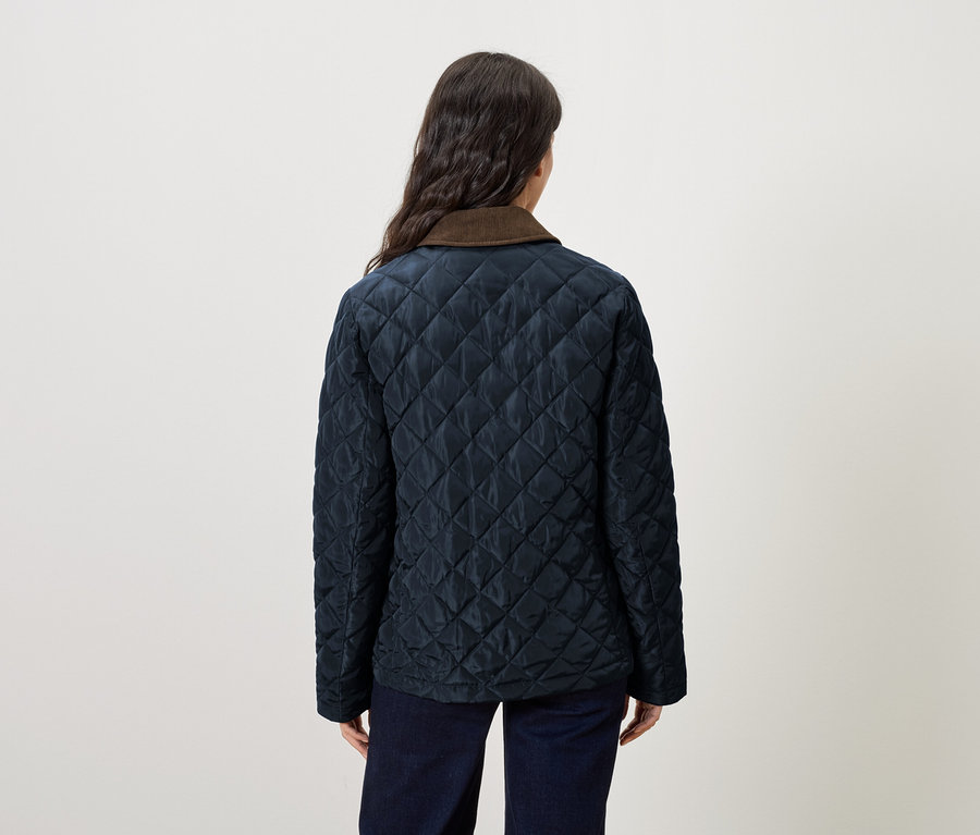 Une femme porte une veste matelassée bleu marine avec un col marron.