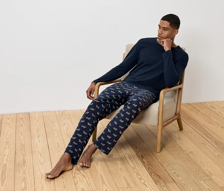Un homme est assis dans un fauteuil et porte un pyjama bleu marine avec un motif de teckels.