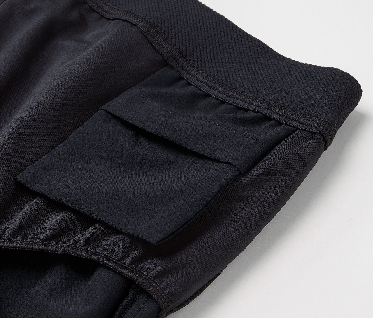 Détail d'un pantalon de sport noir avec une poche sur la cuisse et une taille élastique.