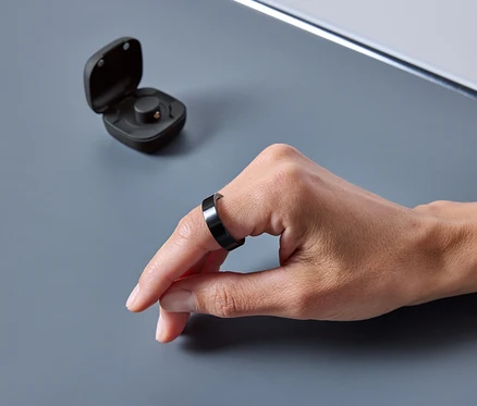 Une main porte une bague noire. Un étui ouvert est à côté de la bague.