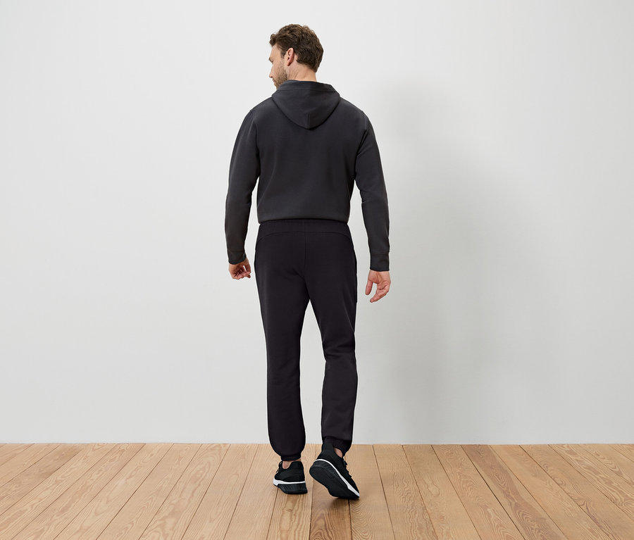 Un homme, vu de dos, porte un sweat à capuche foncé et un pantalon de survêtement noir.