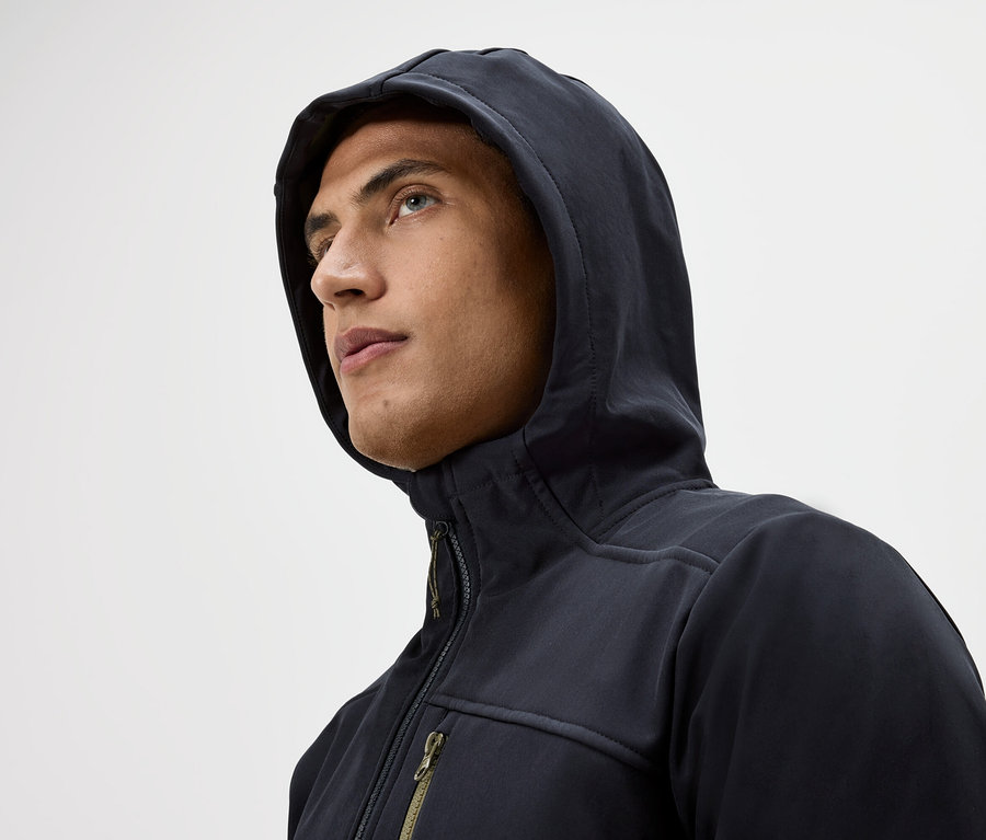Portrait d'un homme portant un sweat à capuche et une veste zippée, regardant vers le haut sur un fond blanc.