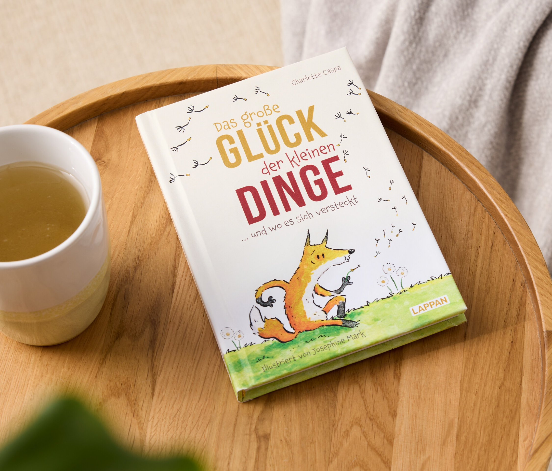Livre "Das große Glück der kleinen Dinge" et une tasse de boisson sur un plateau en bois.