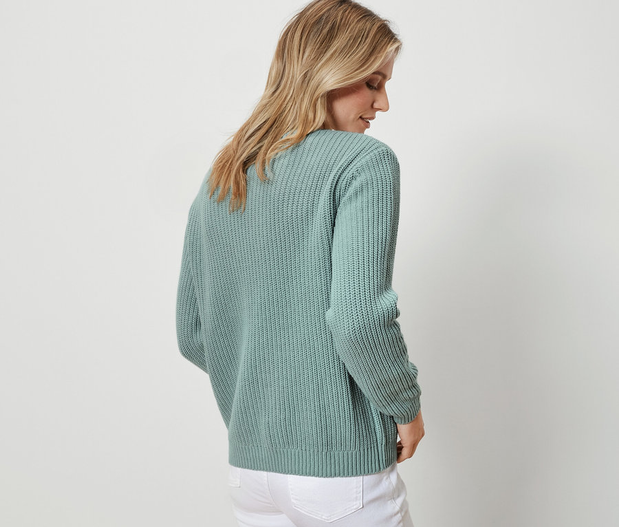 Femme vue de dos portant un cardigan en grosse maille sauge et un jean blanc.