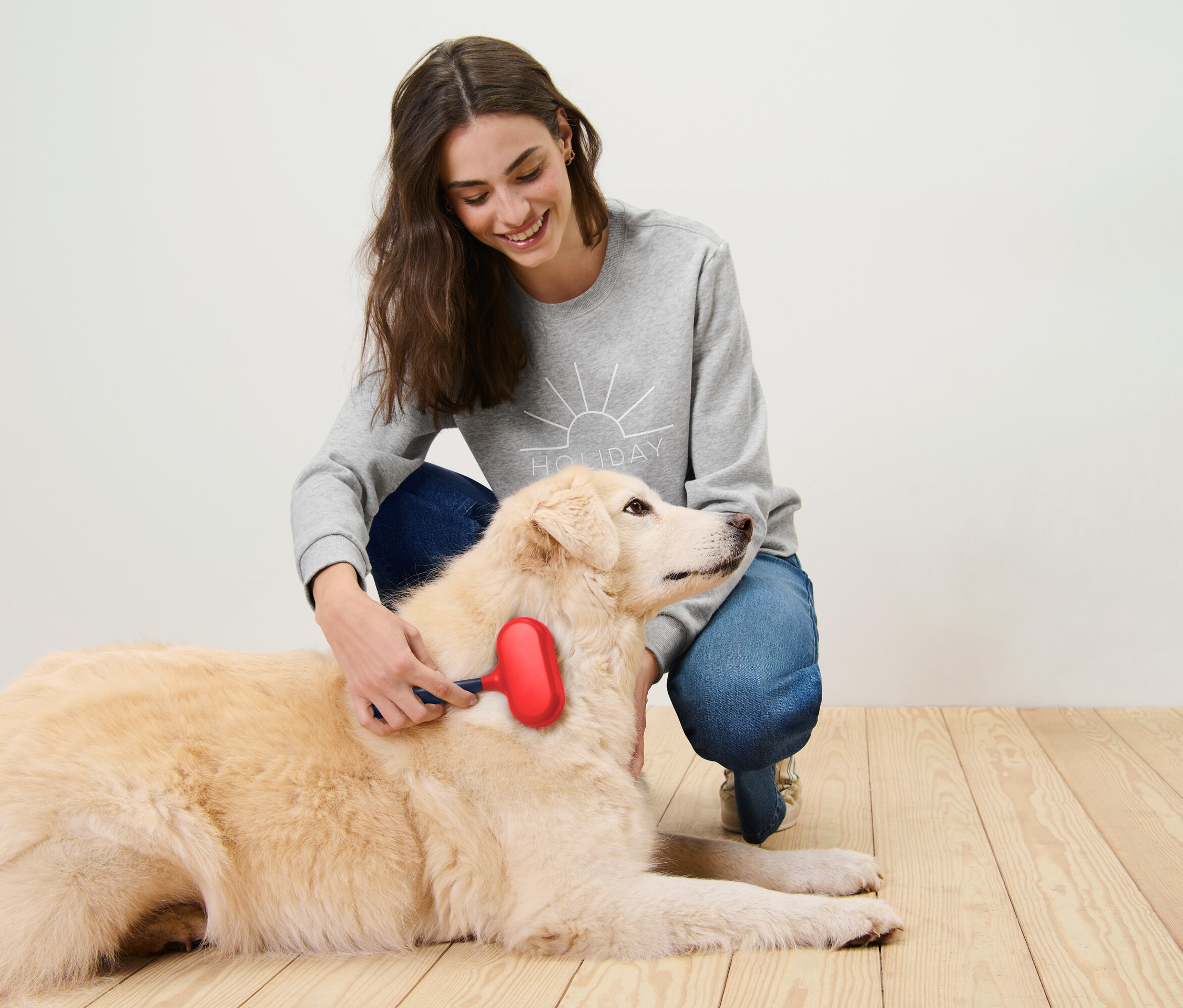 Une femme brosse un chien allongé avec une brosse rouge.