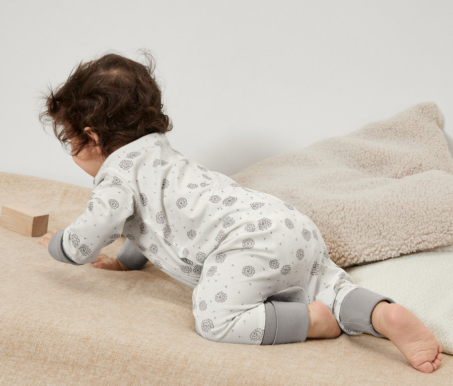 Un bébé rampe sur une couverture beige dans un ensemble de 3 pyjamas pour bébé avec des détails gris et joue avec un bloc de bois.