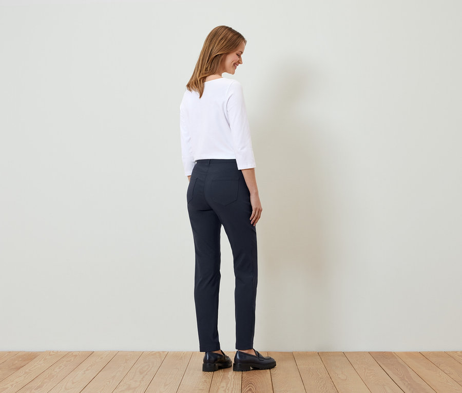 Femme posant dans un haut blanc et un pantalon bleu foncé.