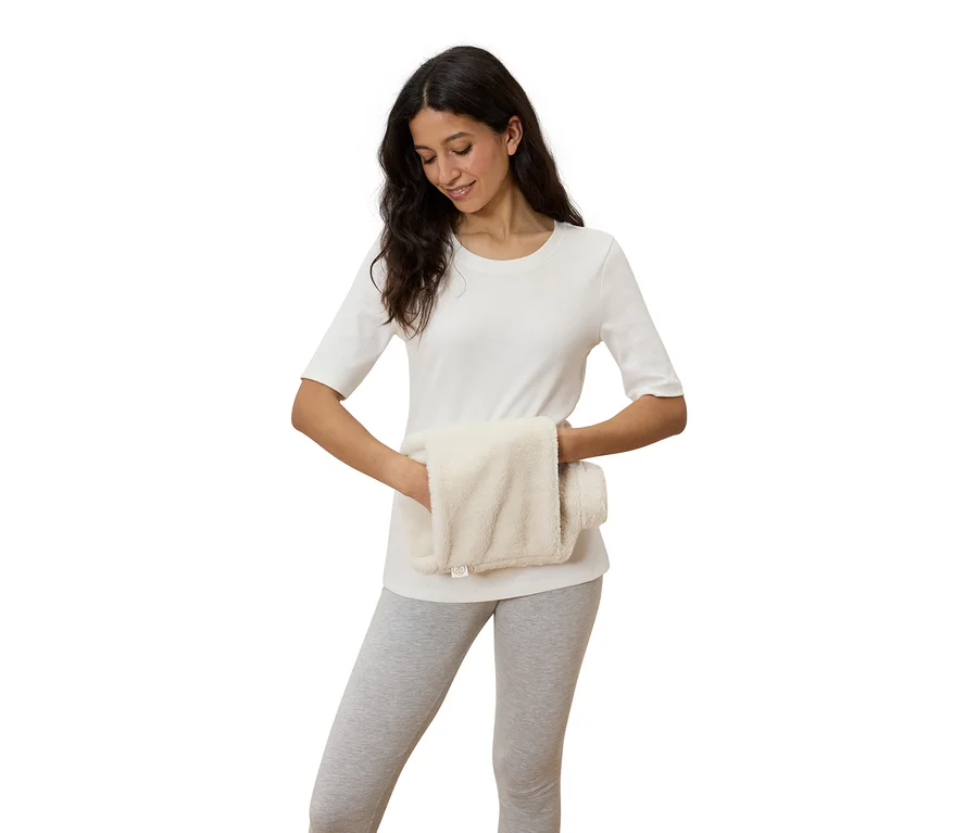Une femme tient un coussin chauffant blanc crème dans ses mains.