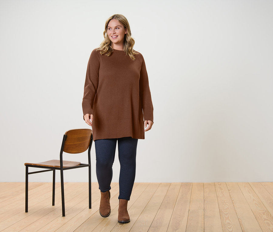 Une femme marche et porte un long pull en maille marron foncé et un legging doublé à l’aspect jean.