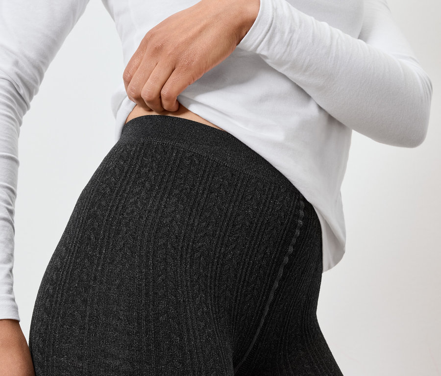 Femme portant des leggings tricotés gris et un t-shirt blanc à manches longues ajustant la taille des leggings.