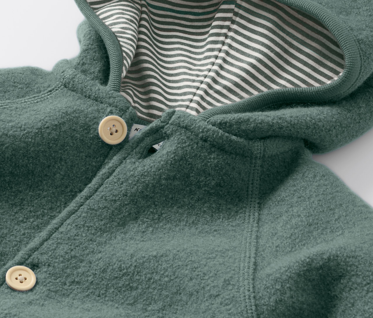Vue détaillée d'une combinaison pour bébé en laine mérinos, fermée par des boutons et dotée d'une capuche avec une doublure rayée.