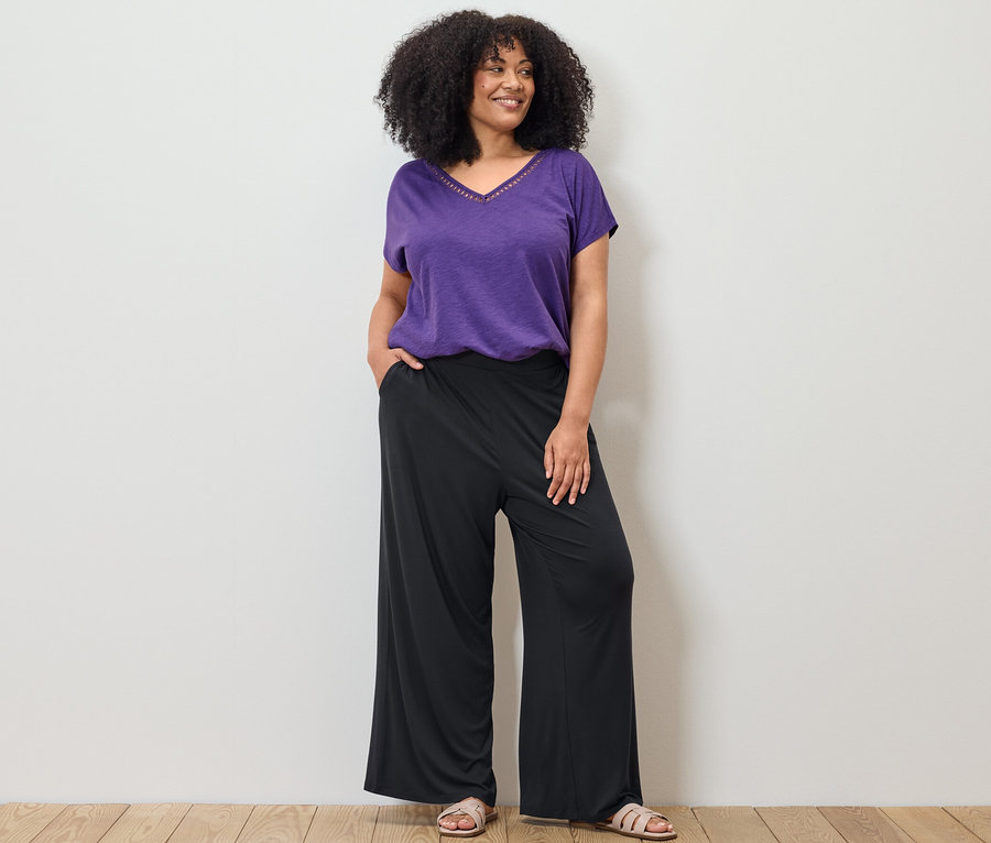 Femme posant en T-shirt en mélange avec modal violet et pantalon palazzo noir.