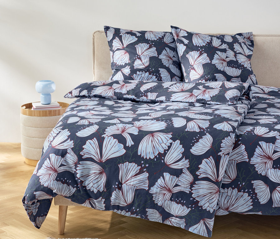 Lit avec des draps bleu marine à motif floral et deux oreillers sur une tête de lit beige.
