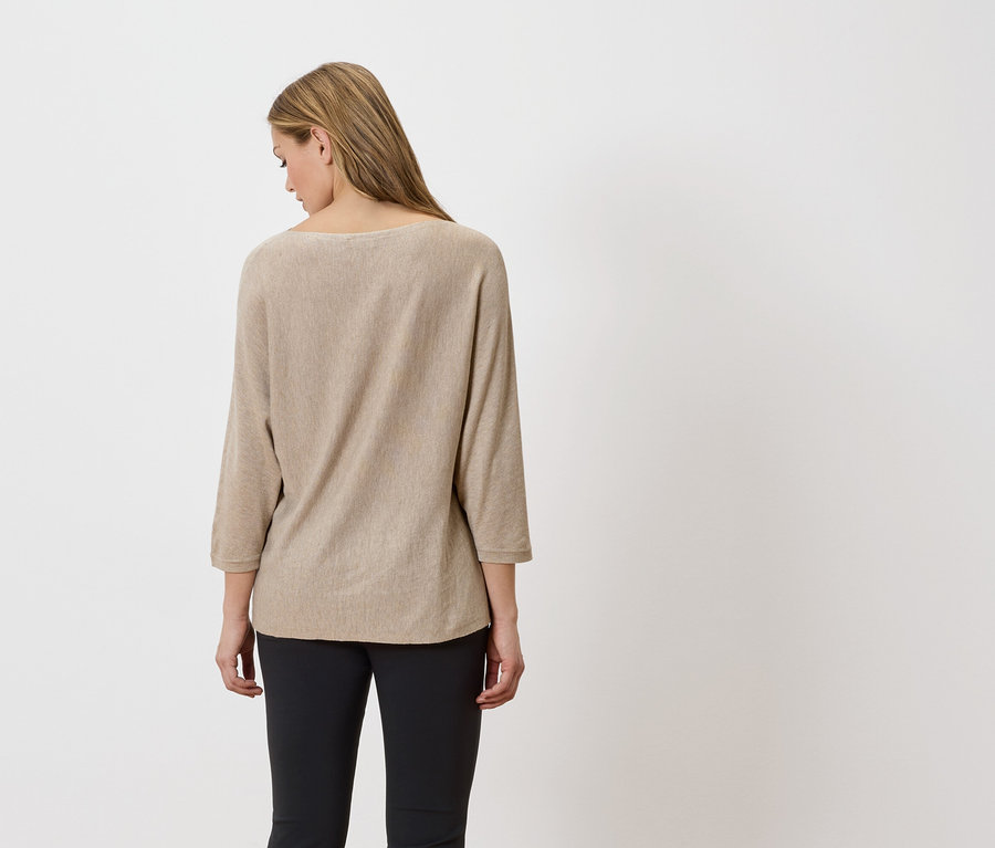 Vue de dos d'une femme blonde portant un pull beige et un pantalon noir.