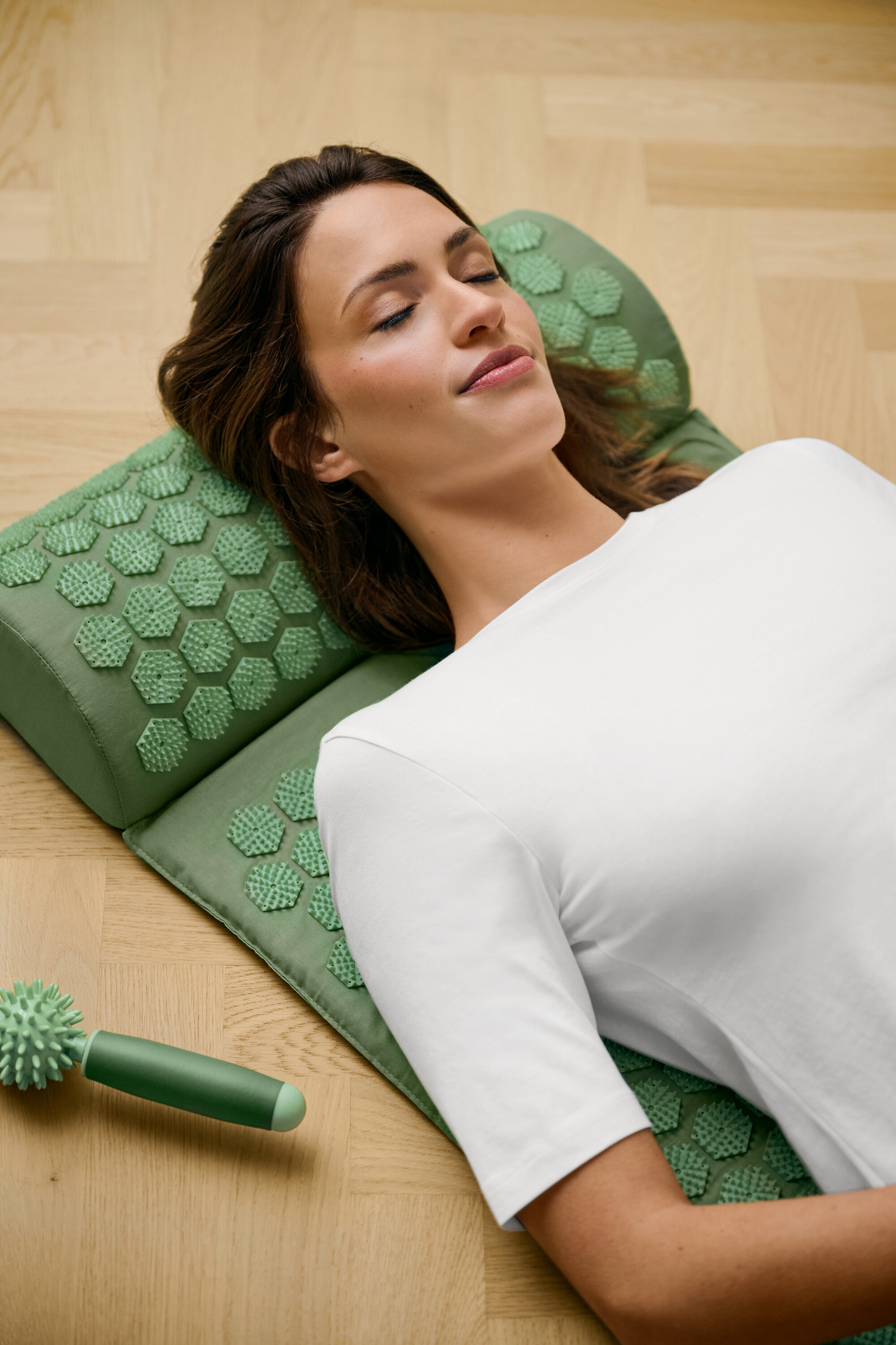 Femme allongée sur un tapis d'acupression vert portant un t-shirt blanc à manches courtes.