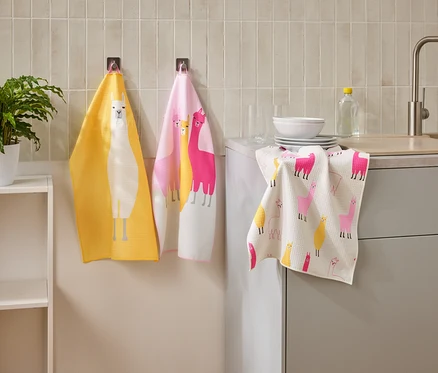 Trois torchons à motifs de lamas sont accrochés dans une cuisine à côté d'un évier et d'une étagère.