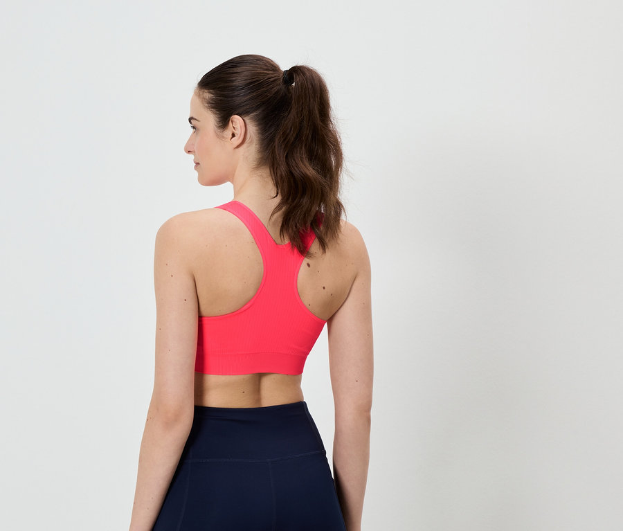 Vue arrière d'une femme portant un soutien-gorge de sport rose et un legging bleu marine, les cheveux attachés en queue de cheval.
