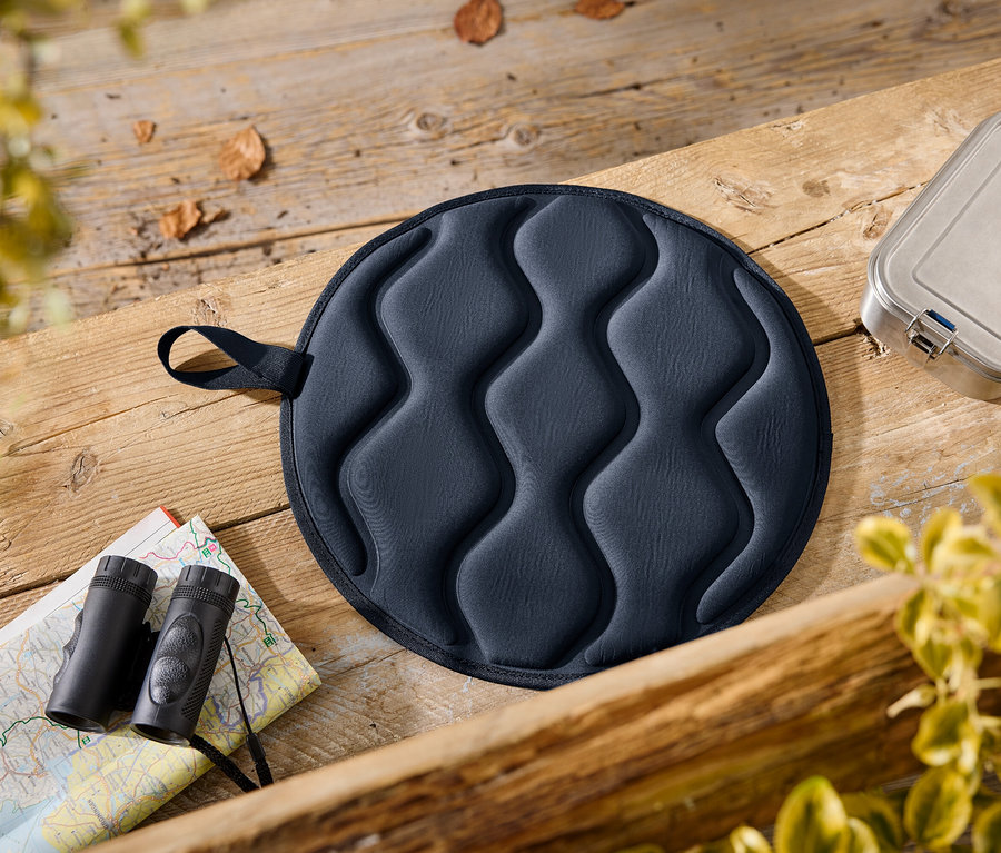 Sur une table en bois reposent un coussin d'assise bleu, une boîte à lunch, une carte et des jumelles.