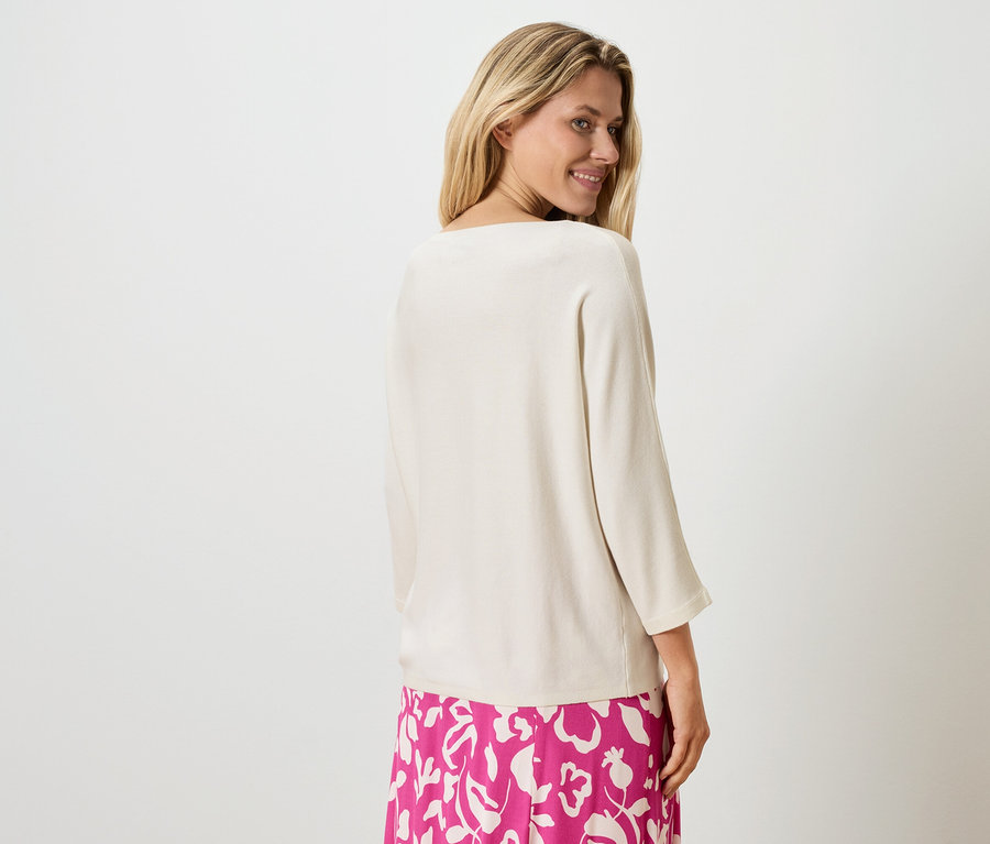 Femme blonde portant un haut beige et une jupe rose à fleurs, regardant par-dessus son épaule.