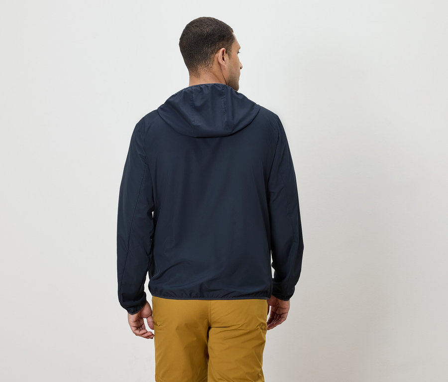 Un homme vu de dos portant une veste bleu marine à capuche et un pantalon jaune.