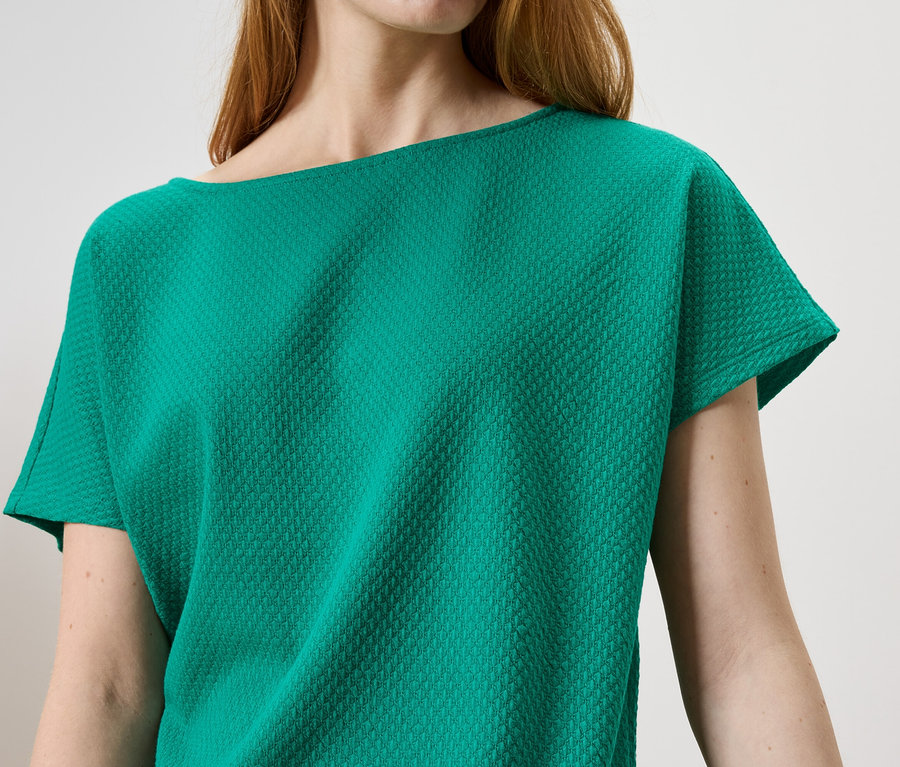Gros plan d'une femme portant un haut vert émeraude avec une surface texturée.
