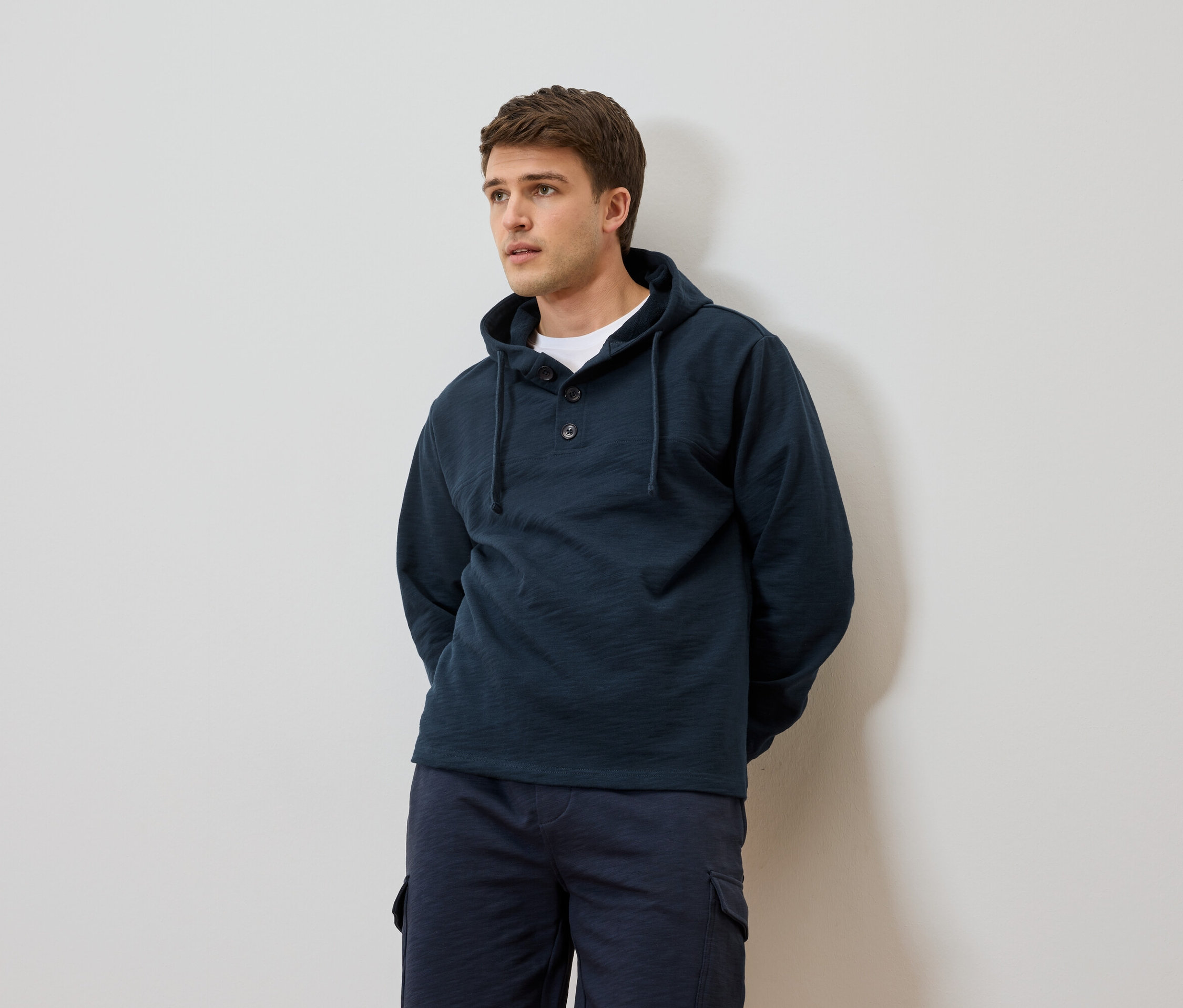 Homme portant un sweat à capuche bleu marine et un short devant un mur blanc.