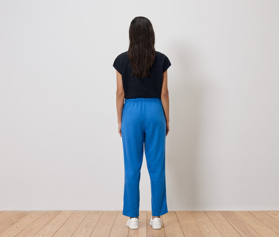 Vue arrière d'une femme aux cheveux foncés portant un t-shirt noir, un pantalon bleu et des baskets blanches.