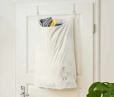 Un sac à linge blanc avec un motif de lama suspendu à une porte blanche.