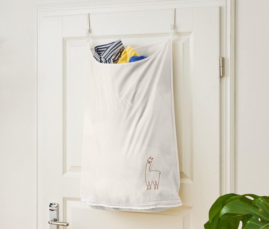 Un sac à linge blanc avec un motif de lama suspendu à une porte blanche.
