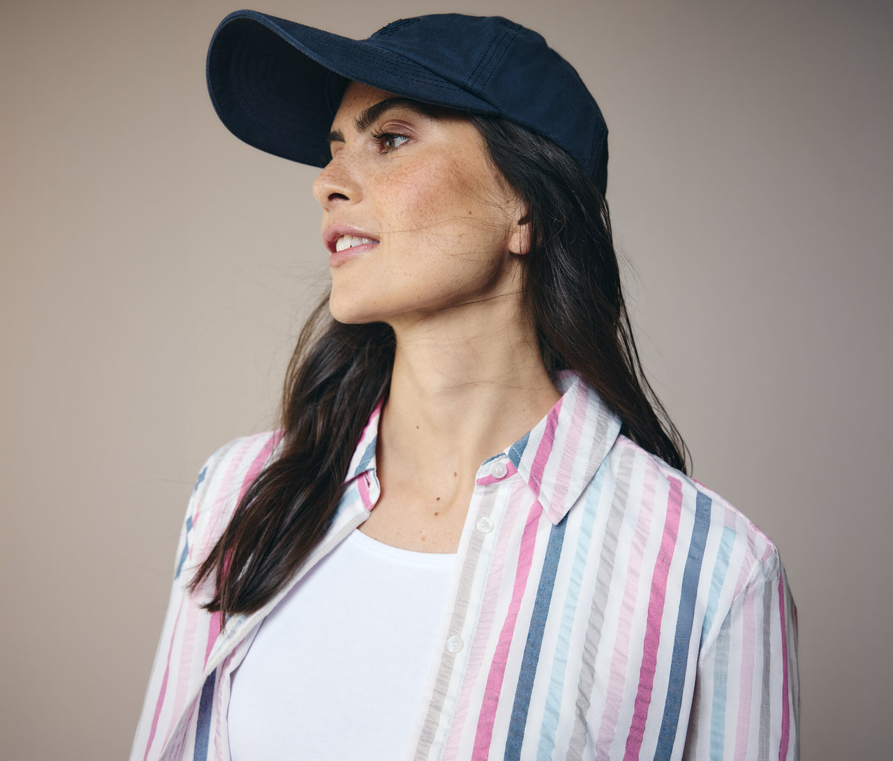 Femme portant une casquette bleu marine et un chemisier CECIL rayé, regardant vers la gauche.