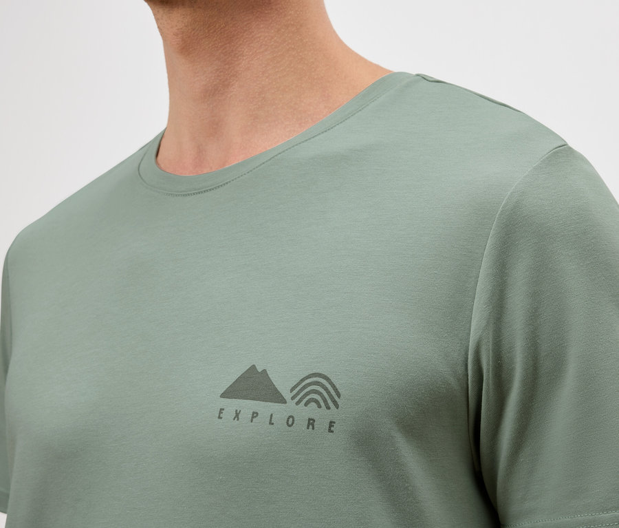 Gros plan d'un homme portant un t-shirt vert clair avec un petit logo "Explore".