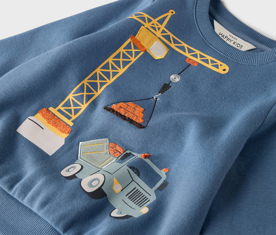 Sur un pull bleu est représentée une grue jaune se tenant au-dessus d'un camion avec des roues.