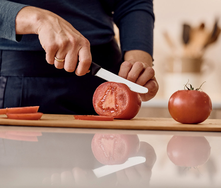 Une personne coupe une tomate avec un couteau sur une planche à découper en bois.