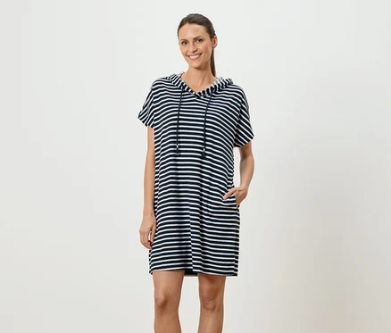 Femme debout, la main dans la poche, portant une robe à capuche rayée bleu et blanc.