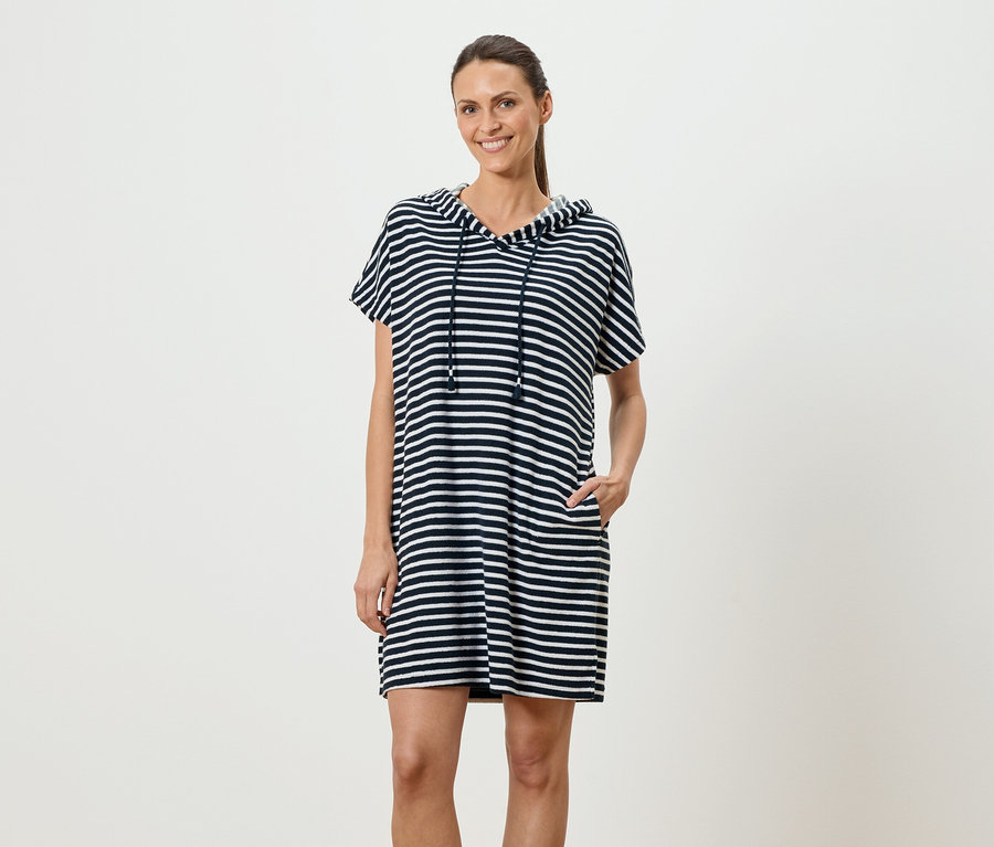 Femme debout, la main dans la poche, portant une robe à capuche rayée bleu et blanc.