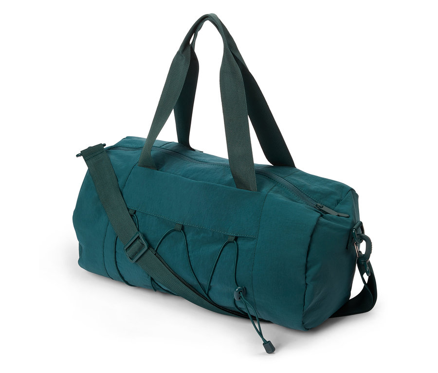 Sac de sport vert avec poignées et bandoulière posé sur le sol.