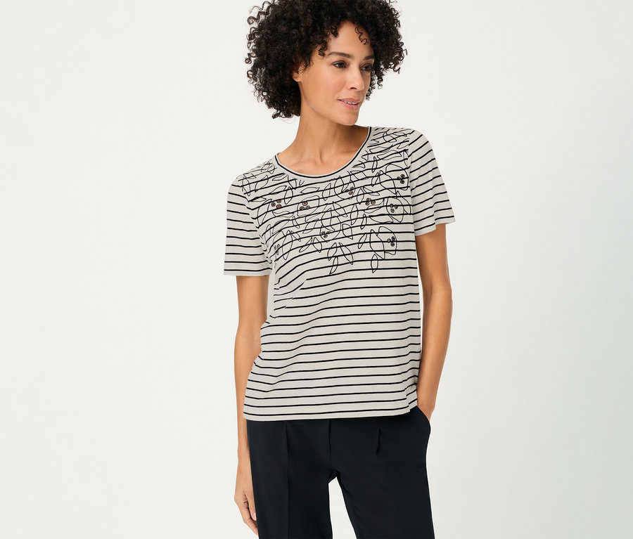 Une femme aux cheveux bouclés porte un T-shirt Olsen rayé avec un motif floral et un pantalon foncé.