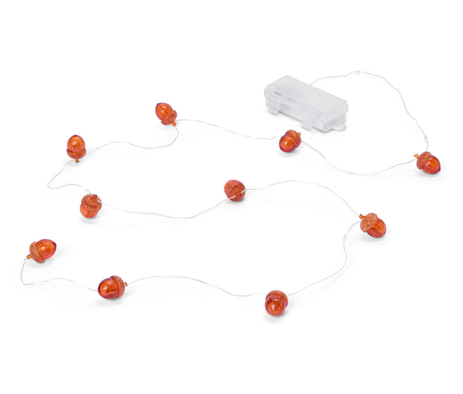 Une guirlande lumineuse avec des glands couleur ambre et un boîtier de piles transparent repose sur un fond blanc.